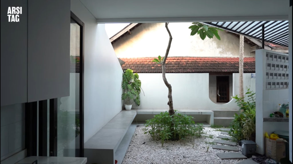 Kebun belakang dengan seating area permanen dan alas lantai bebatuan kecil, via Saturasi Architect